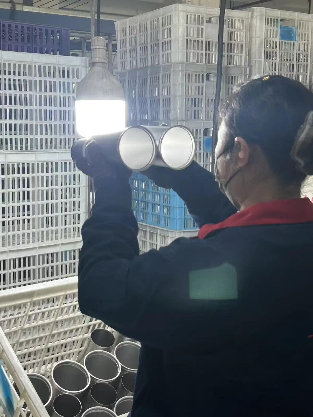Inspector examining tumbler inner walls or weld areas under direct light at a MOWXI-owned or affiliated factory site