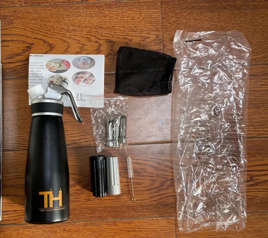 Black cream whipper, included accessories, instruction leaflet and protective packing components arranged as one complete configuration