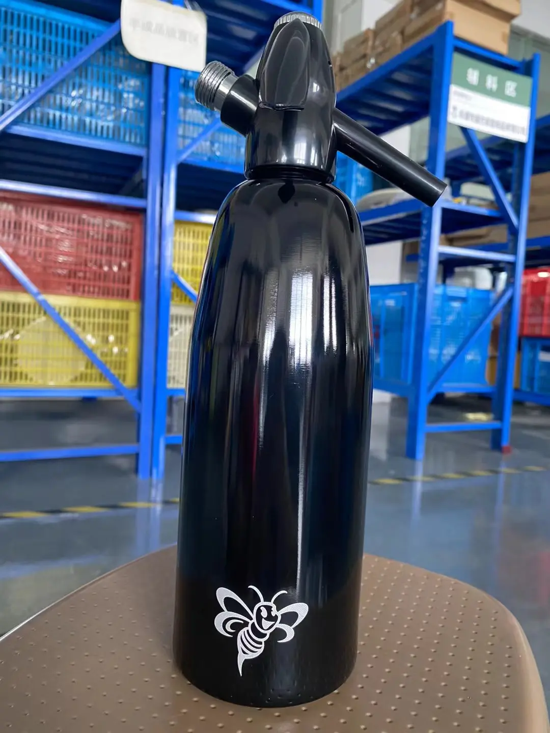 Black soda siphon with a custom logo marked on the body, photographed in a warehouse
